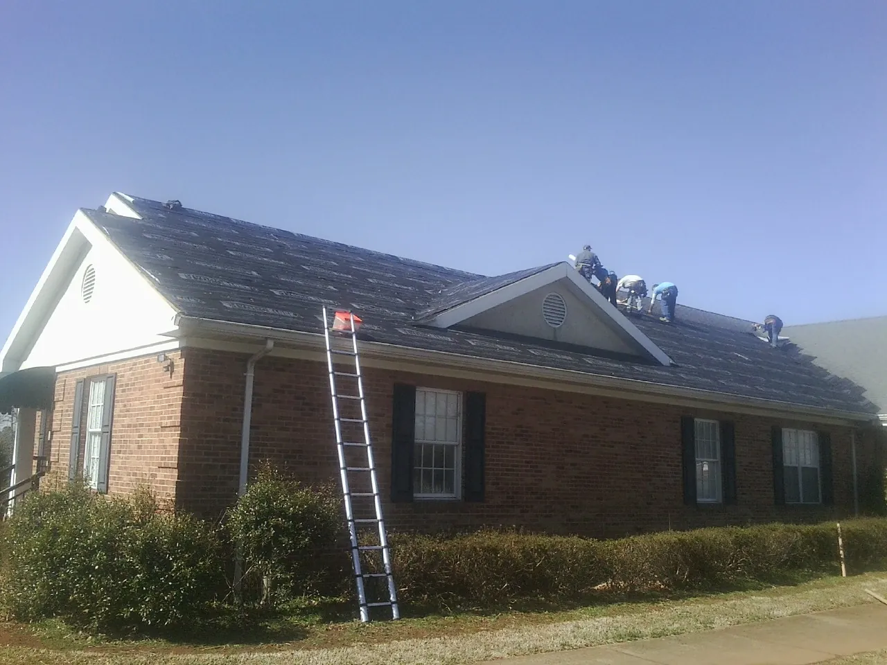 Crew tearing shingles off a brick ranch roof with a ladder set — Emergency Roof Repair work by our crew in Rockhill Furnace