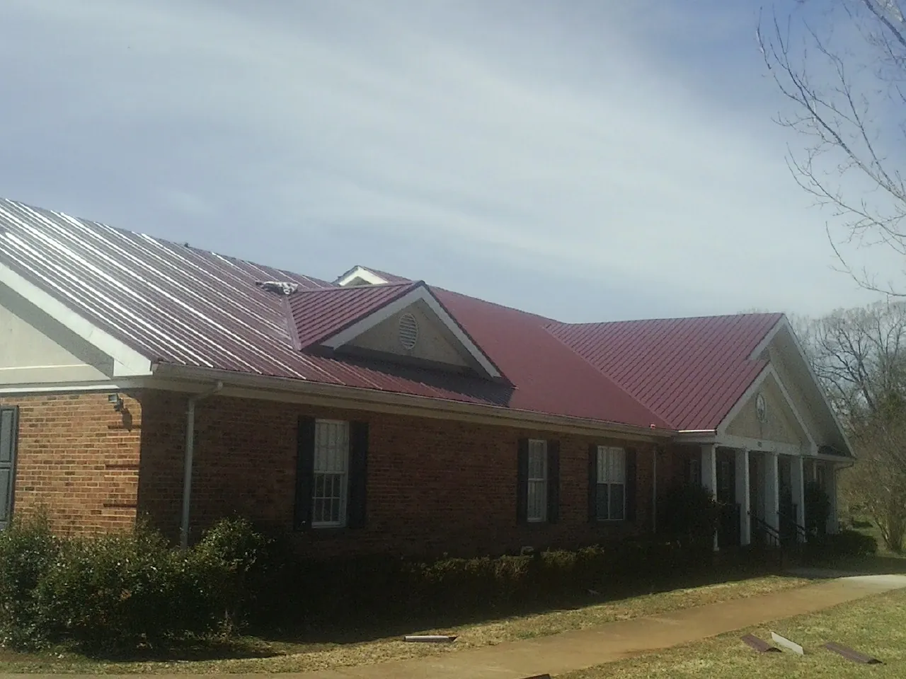 Red metal roof with gabled entries on a long brick building, from a Hail Damage Roof Repair job in Rockhill Furnace