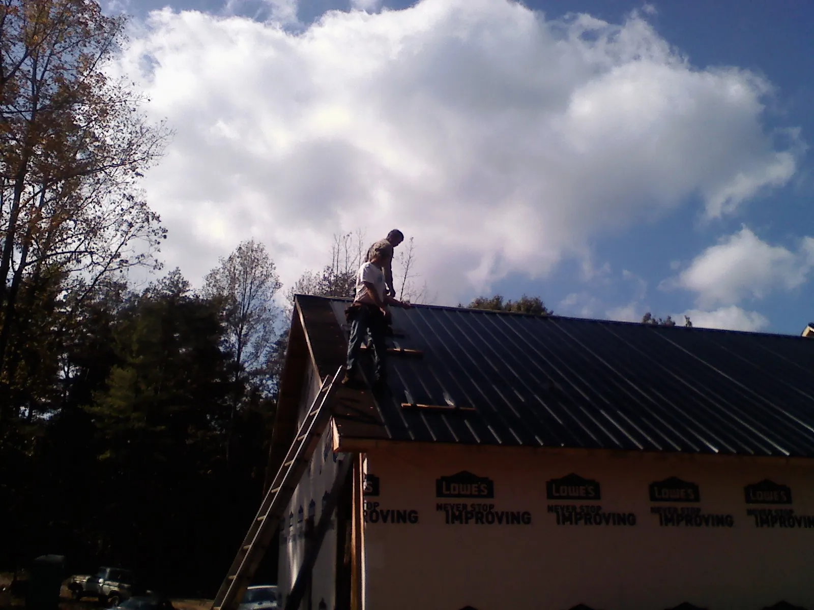 Roofer fastening dark metal panels high against a cloudy sky, from a Roof Inspection job in Rockhill Furnace