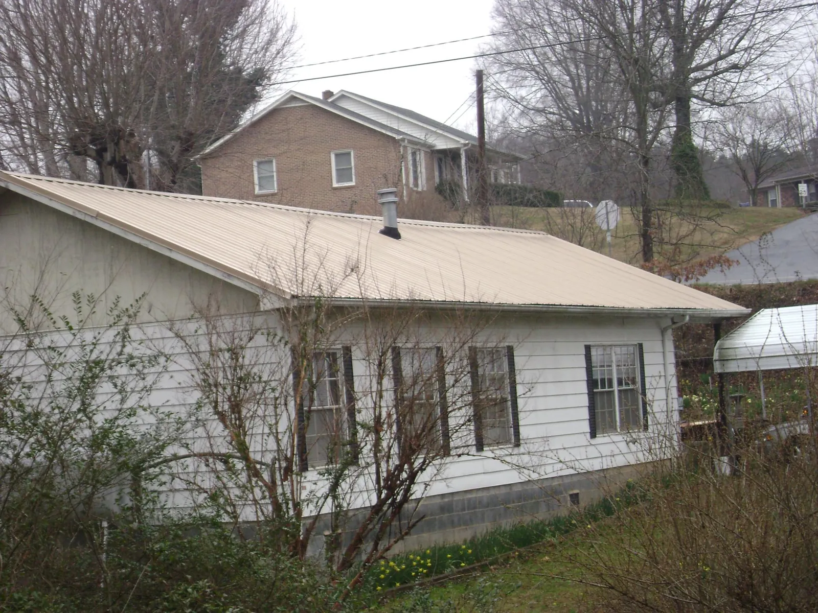 Tan metal roof on a white sided house set into a hillside — Commercial Roofing by Roofing Brothers in Rockhill Furnace